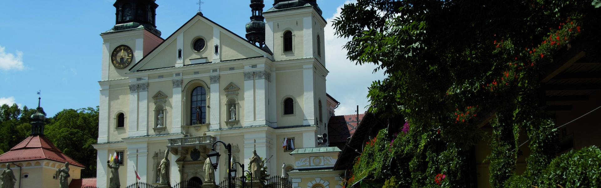 Klasztor Bernarydynów w Kalwarii Zebrzydowskiej, z dwoma wieżami po bokach, przed nim plac i turyści