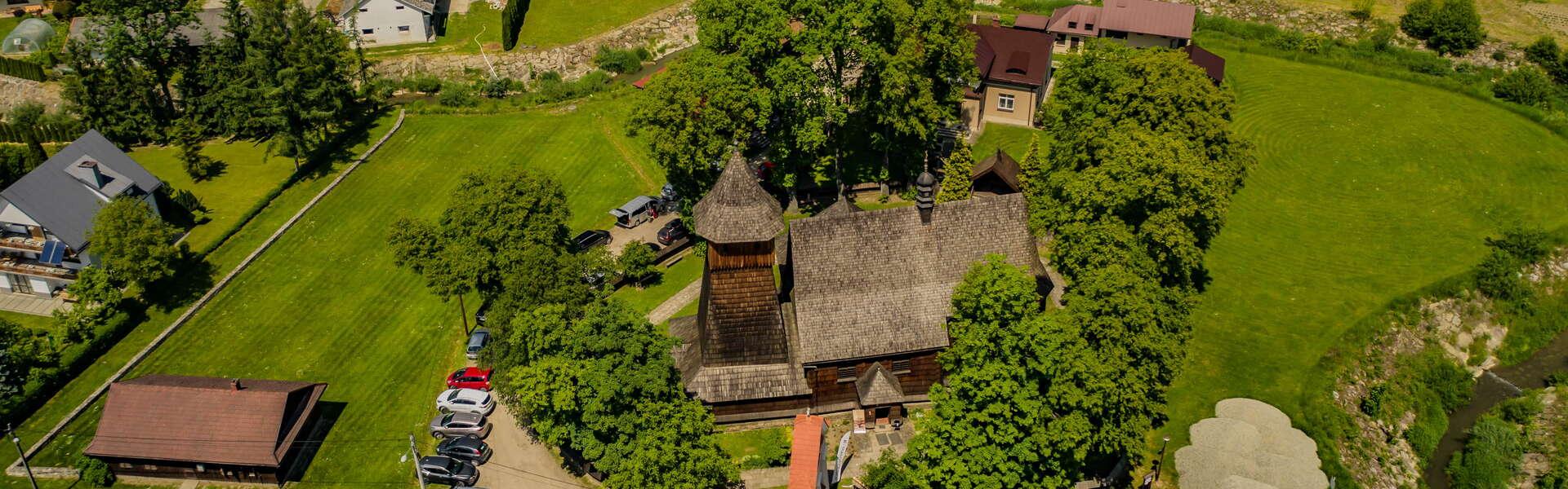 Drewniany kościół wśród zieleni widziany z lotu ptaka.